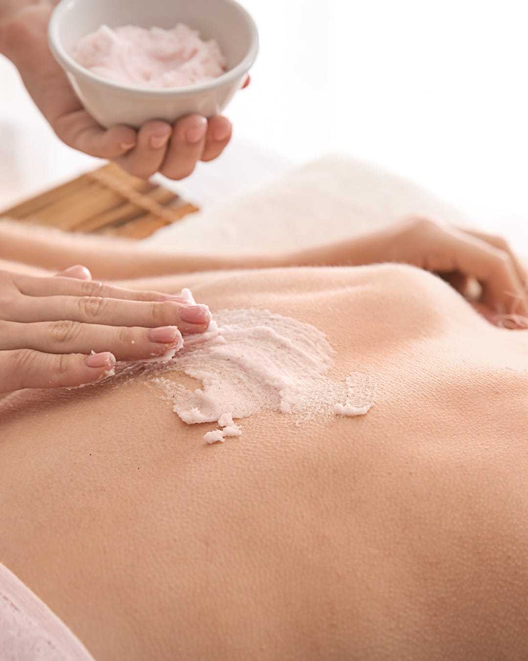 Skincare treatment with pink scrub being applied to a person's back.