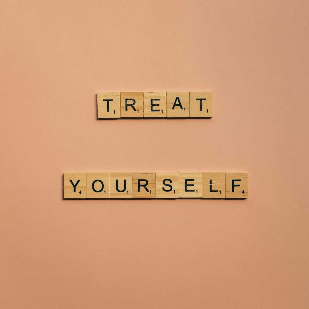 Scrabble tiles spell out "Treat Yourself" on a peach-colored background.
