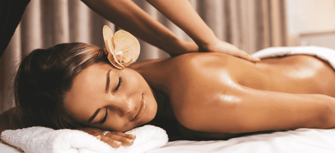 Woman receiving a relaxing back massage with a flower in her hair at a spa.